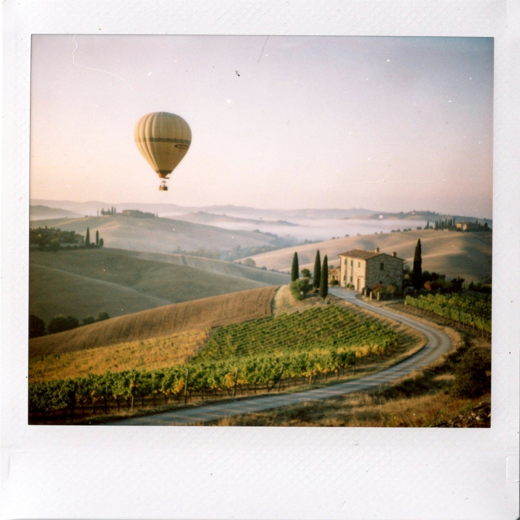 A vintage hot air balloon drifting over rolling Tuscan hills at dawn, taken from a polaroid
